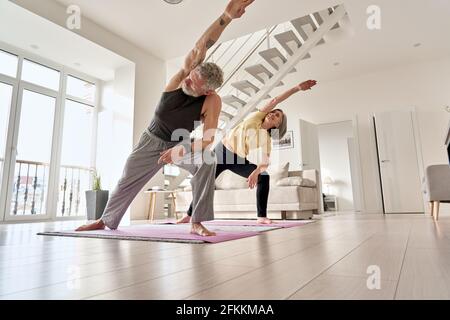 Fit middle aged family couple doing fitness morning exercise at home. Stock Photo