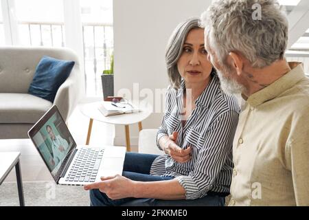 Mature old grandparents couple having video chat with virtual doctor at home. Stock Photo