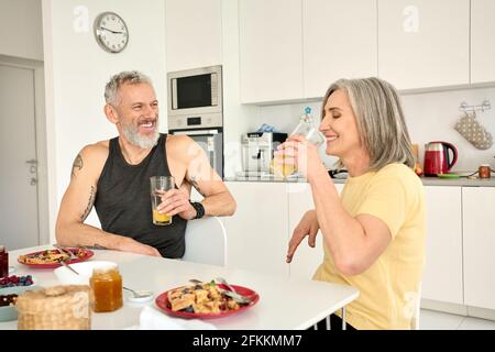 Happy healthy fit senior family couple having breakfast sit at kitchen table. Stock Photo