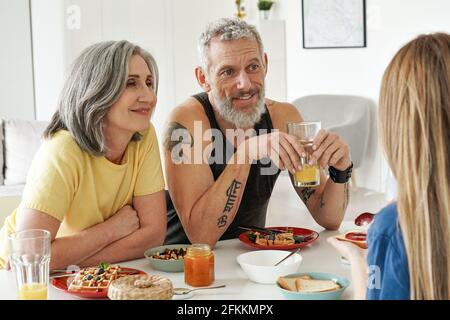 Happy older family couple having breakfast with daughter sit at kitchen table. Stock Photo