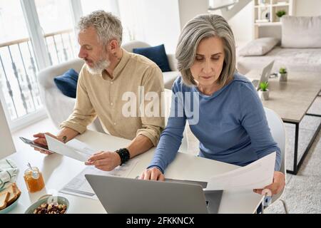 Mature couple reading documents bills paying bank loan using laptop and phone. Stock Photo