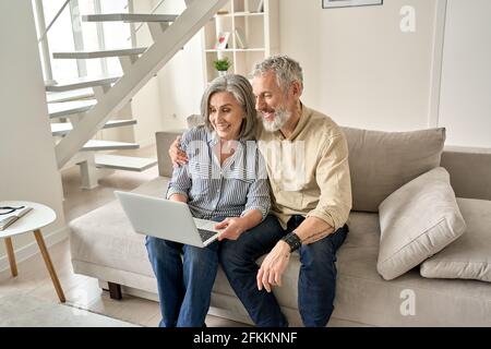Happy old mid age family couple using laptop computer sitting on couch. Stock Photo