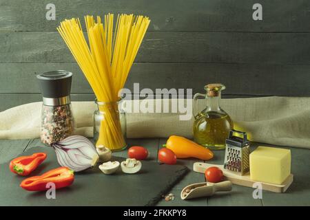 Raw dry Italian spaghetti and fresh vegetables. Spaghetti pasta, vegetables and spices and cheese on a wooden table. Background with space for text