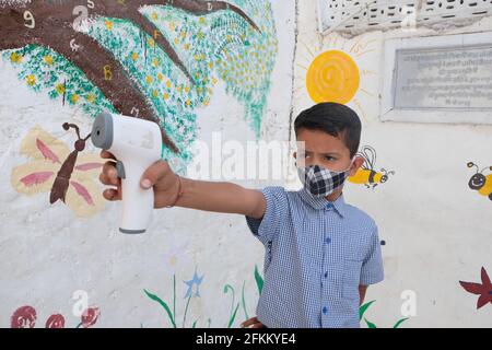 An Indian schoolboy wearing a face mask and uniform using a digital thermometer during Covid-19 Stock Photo