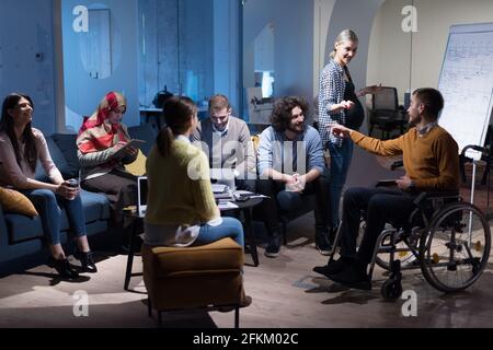 Disabiliti concept. Diverse group of architects with one in wheelchair working in coworking office using modern technology. Stock Photo