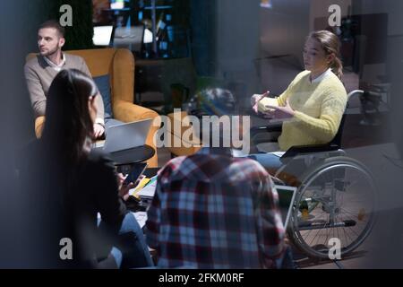Office workers and person in a wheelchair discussing business moments in a modern office. Disability and business concept Stock Photo