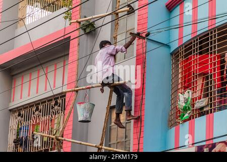 RAJSHAHI, BANGLADESH - NOVEMBER 10, 2016: Worker on a dangerous bamboo scaffolding paints a building in Rajshahi, Bangladesh Stock Photo