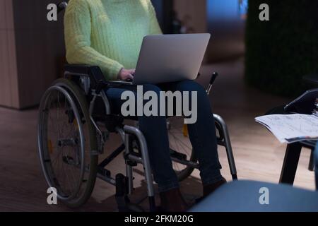 Young woman in wheelchair using computer laptop at modern workplace Stock Photo