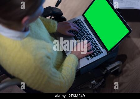Young woman in wheelchair using computer laptop at modern workplace Stock Photo