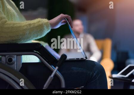 Young woman in wheelchair using computer laptop at modern workplace Stock Photo