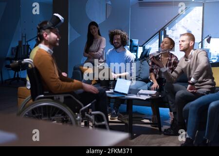 Disabiliti concept. Diverse group of architects witho one in wheelchair working in coworking office using modern technology. Stock Photo