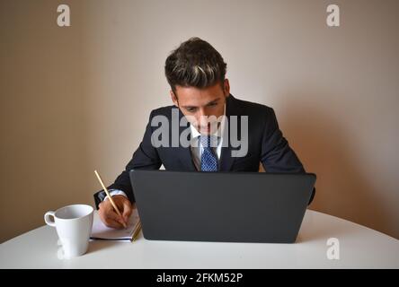 A caucasian businessman in a suit taking notes while working on his lapto Stock Photo