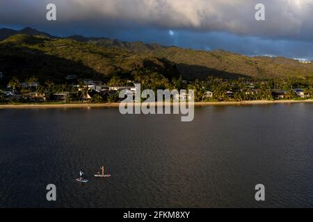 Two people on stand up paddlboards in the ocean in front of a mountain Stock Photo