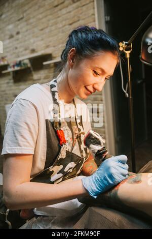 Portrait of a woman tattoo master showing a process of creation tattoo on a hand under the lamp light. Stock Photo