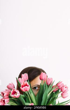 Close-up of woman hiding behind tulips against white wall Stock Photo