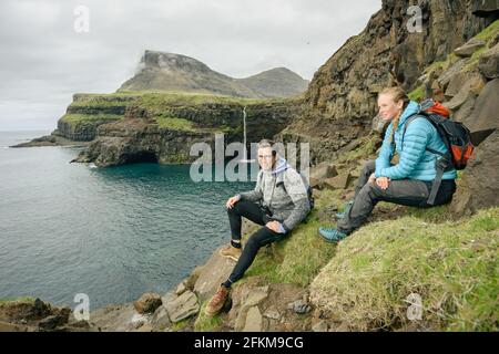 Young travelers sitting on mossy cliff Stock Photo