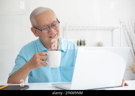Happy senior man working on laptop and holding coffee cup Stock Photo