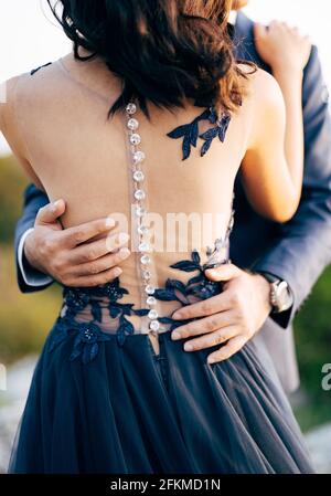 Groom in a blue suit hugs bride in a blue dress by the waist. Close up. Back view Stock Photo