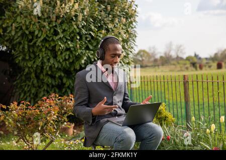 An african american businessman during a work video call wears his headphones and talks outdoors in a garden Stock Photo