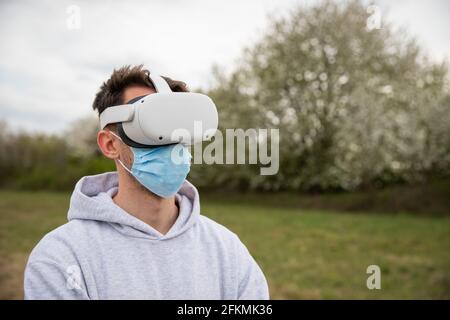 A man uses virtual reality headset outside, wearing a surgical mask Stock Photo