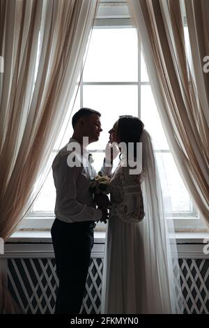 Cute portrait of the bride and groom by the window. Wedding photo session. Stock Photo
