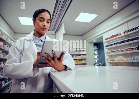 Low angle view of young female woman wearing labcoat working in chemist using digital tablet to confirm online order Stock Photo