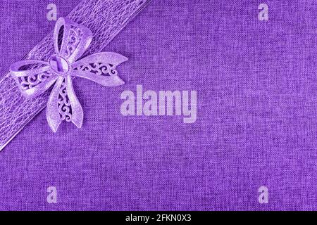 Elegant shiny purple glitter bow on purple colored ribbon and on bright purple burlap. Horizontal greeting card background with large copy space and d Stock Photo