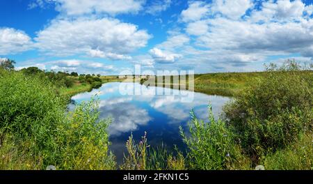Beautiful panoramic rural landscape with calm river and green hills with trees at sunny summer day. Stock Photo