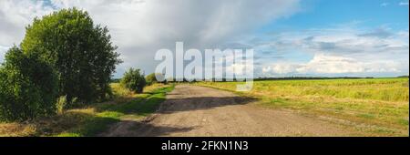 Sunny summer landscape with dirt rural road passing through the fields and meadows. Stock Photo