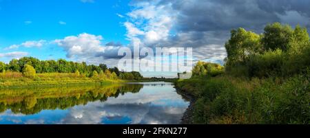 Stormy dramatic sky over the calm lake and green hills during sunset.Beautiful panoramic landscape.Beauty of evening nature. Stock Photo