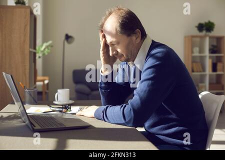 Troubled mature businessman sitting at desk and looking at laptop computer screen Stock Photo