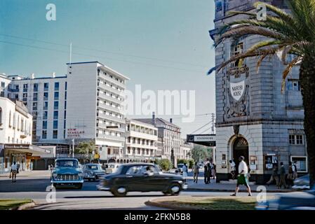 A view looking down Kenyatta Avenue at Mio Avenue, downtown Nairobi, Kenya, Africa in 1959. Left is the New Stanley Hotel (now the Sarova Stanley Hotel). Right is the colonial architecture of Nairobi House, since demolished. Nairobi is the capital and the largest city of Kenya. The name comes from the Maasai phrase Enkare Nairobi, which translates to ‘cool water’, a reference to the Nairobi River which flows through the city. This image is from an old amateur 35mm Kodak colour transparency. It has motion blur from the moving cars and people – a vintage 1950s photograph. Stock Photo