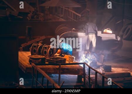 Worker welding metal parts at metallurgical plant, processing metal after casting. Stock Photo