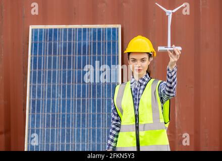 factory workers or engineers holding light bulb and using tablet computer with windmill model on solar panel,  work in containers warehouse storage Stock Photo