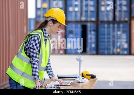factory workers or engineers holding light bulb and using tablet computer with windmill model on solar panel,  work in containers warehouse storage Stock Photo