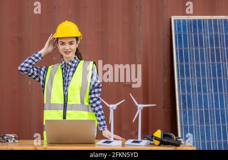 factory workers or engineers holding light bulb and using tablet computer with windmill model on solar panel,  work in containers warehouse storage Stock Photo