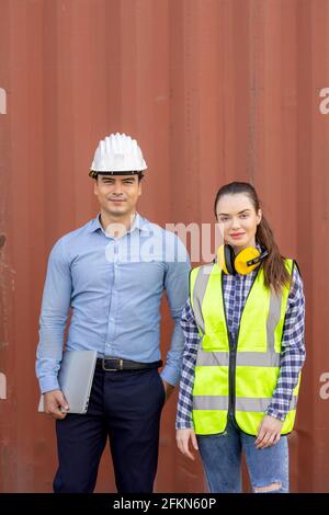 Confident engineers portrait in uniforms standing in front of the containers. Logistics and shipping. Professional occupation. Stock Photo
