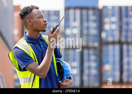 Man Using Walkie Talkie At Container Terminal, Industrial worker is controlling container loading Stock Photo