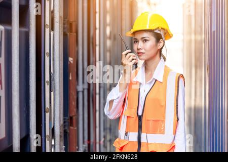 Portrait of Asian worker woman in safety uniform talking with walkie talkie to control work quality at container warehouse. working for logistic and s Stock Photo