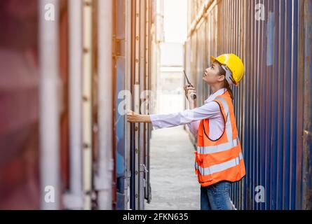 Portrait of Asian worker woman in safety uniform talking with walkie talkie to control work quality at container warehouse. working for logistic and s Stock Photo