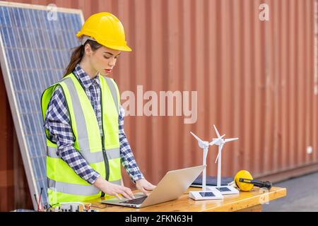 factory workers or engineers holding light bulb and using tablet computer with windmill model on solar panel,  work in containers warehouse storage Stock Photo
