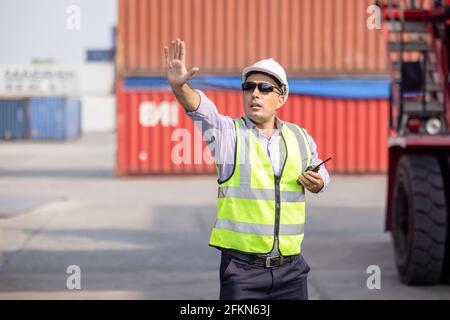 Man Using Walkie Talkie At Container Terminal, Industrial worker is controlling container loading Stock Photo