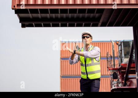 Man Using Walkie Talkie At Container Terminal, Industrial worker is controlling container loading Stock Photo