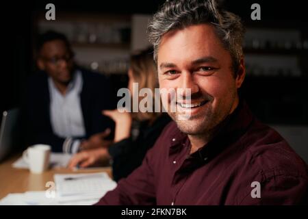 Close-up of smiling mature businessman looking at camera with colleagues at background Stock Photo