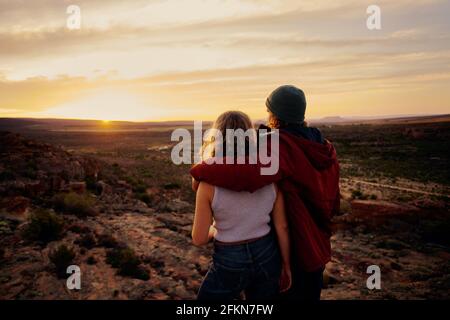 Rear view of young couple enjoying together watching beautiful sunrise standing on mountain Stock Photo