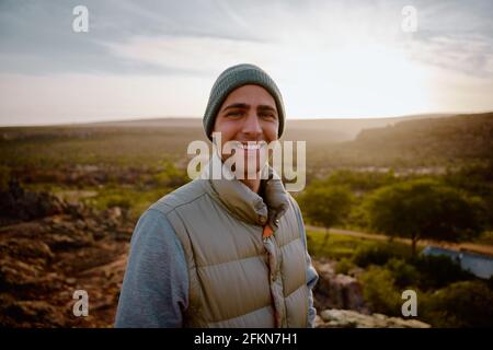 Portrait of cheerful young male hiker looking satisfied after reaching cliff of mountain looking at camera Stock Photo