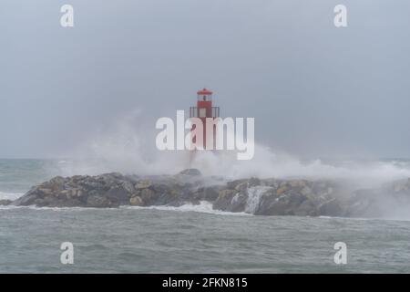 Waves crashing on breakwater with lighthouse in Imperia harbour, Italy