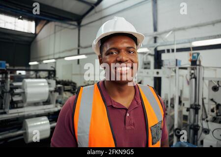 Smiling portrait of a young male factory worker wearing helmet in warehouse Stock Photo
