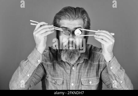 Man eat sushi chopsticks. Sushi rolls. Eastern culture. Bearded hipster eating rolls. Japanese food delivery. Pickled ginger served with sushi or Stock Photo