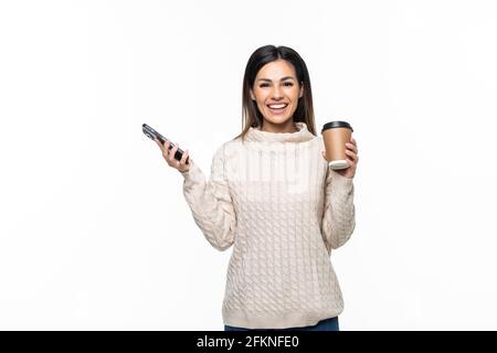 Portrait of a smiling young woman holding mobile phone while drinking coffee and looking at camera isolated over white background Stock Photo